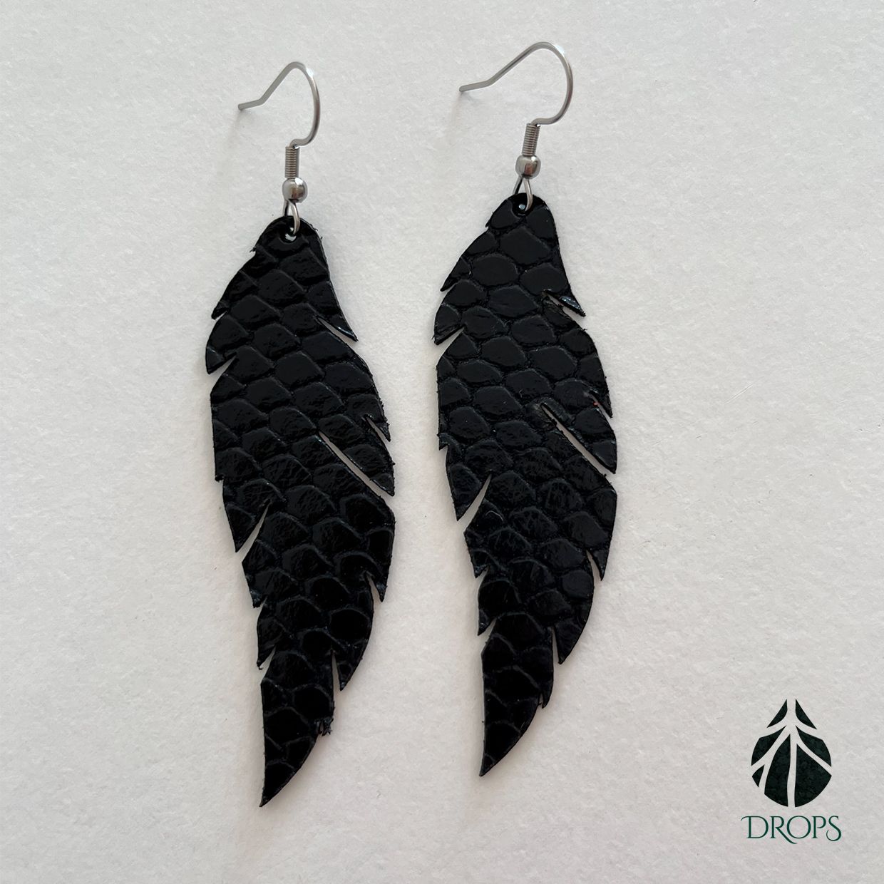 Un par de pendientes negros en forma de plumas hechos con gotas.