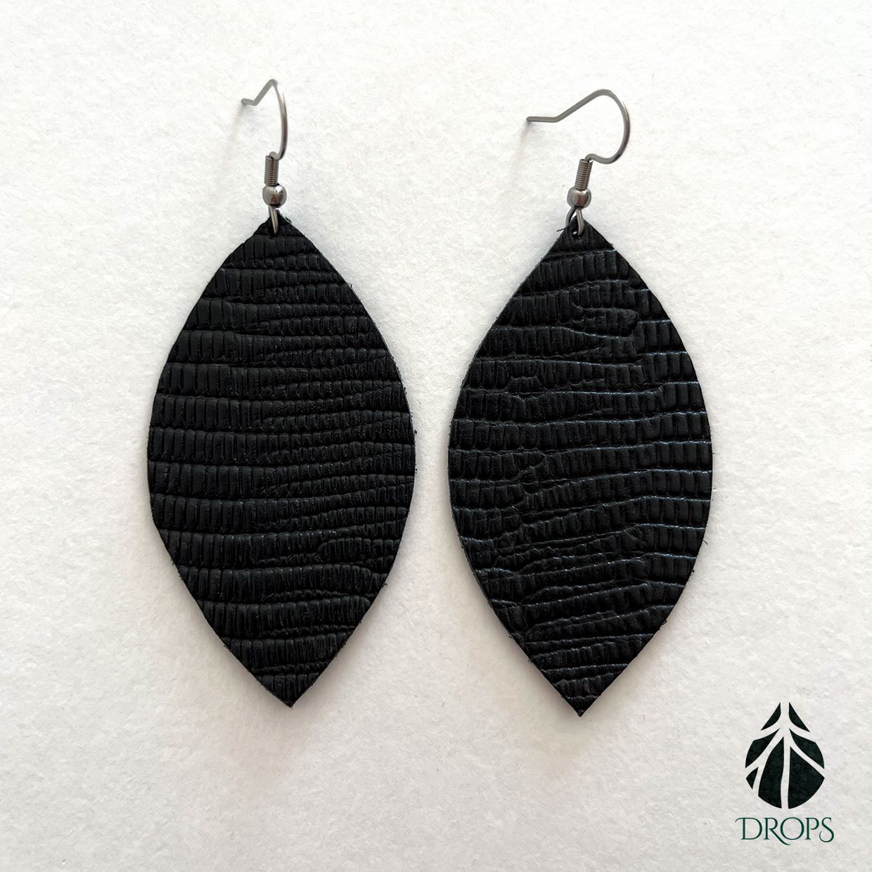 Un par de pendientes negros en forma de hoja hechos con gotas.