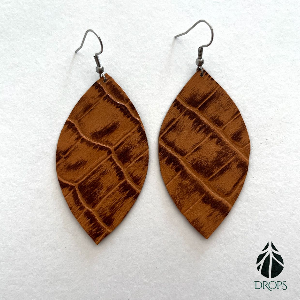 Un par de pendientes marrones en forma de hoja hechos con gotas.