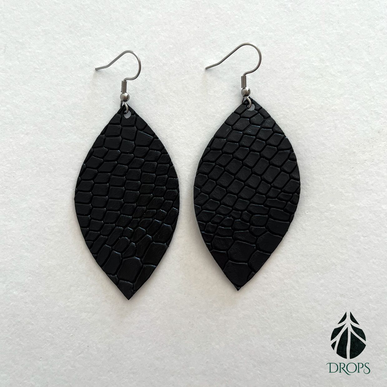 Un par de pendientes negros en forma de hoja hechos con gotas.