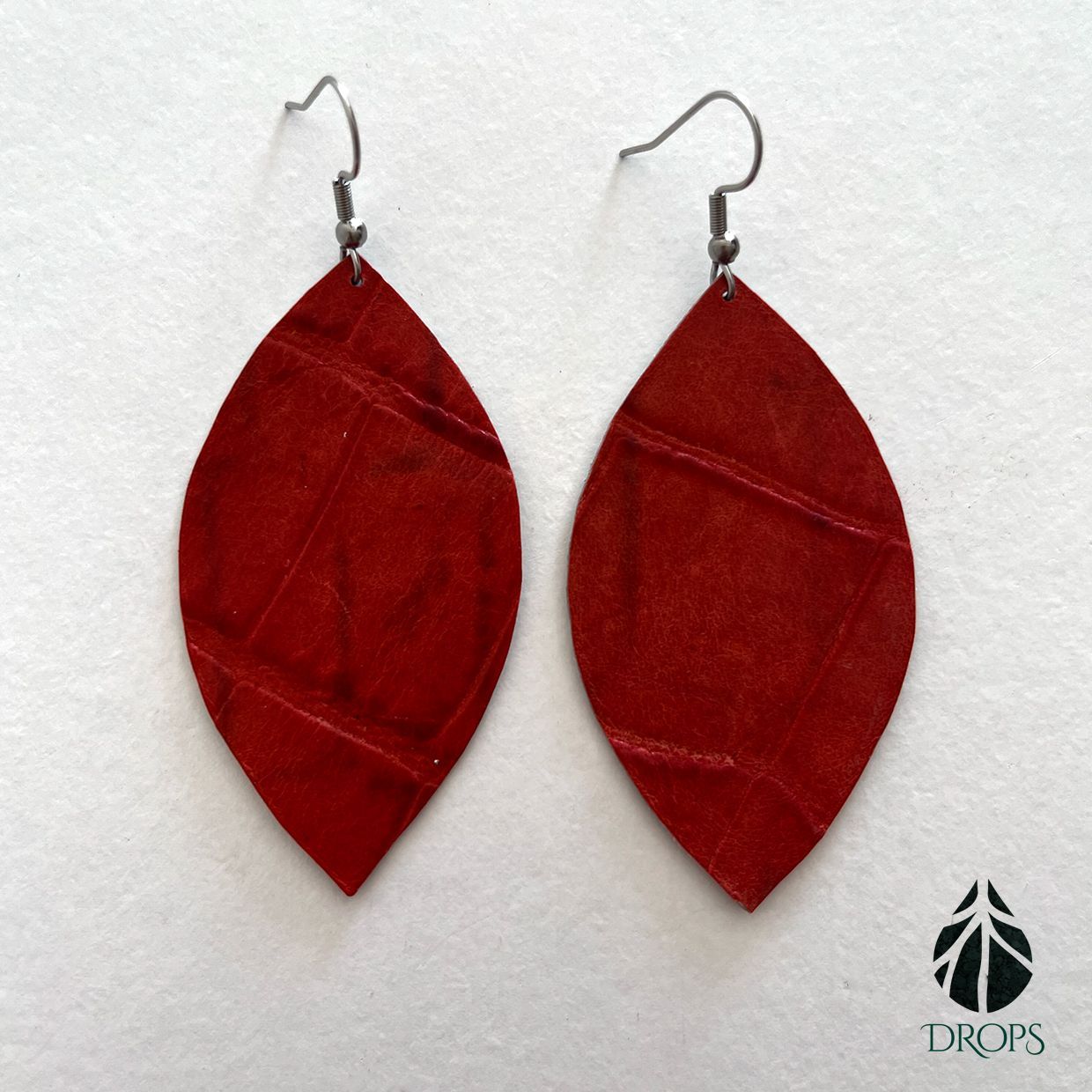 Un par de pendientes en forma de hoja roja hechos con gotas.