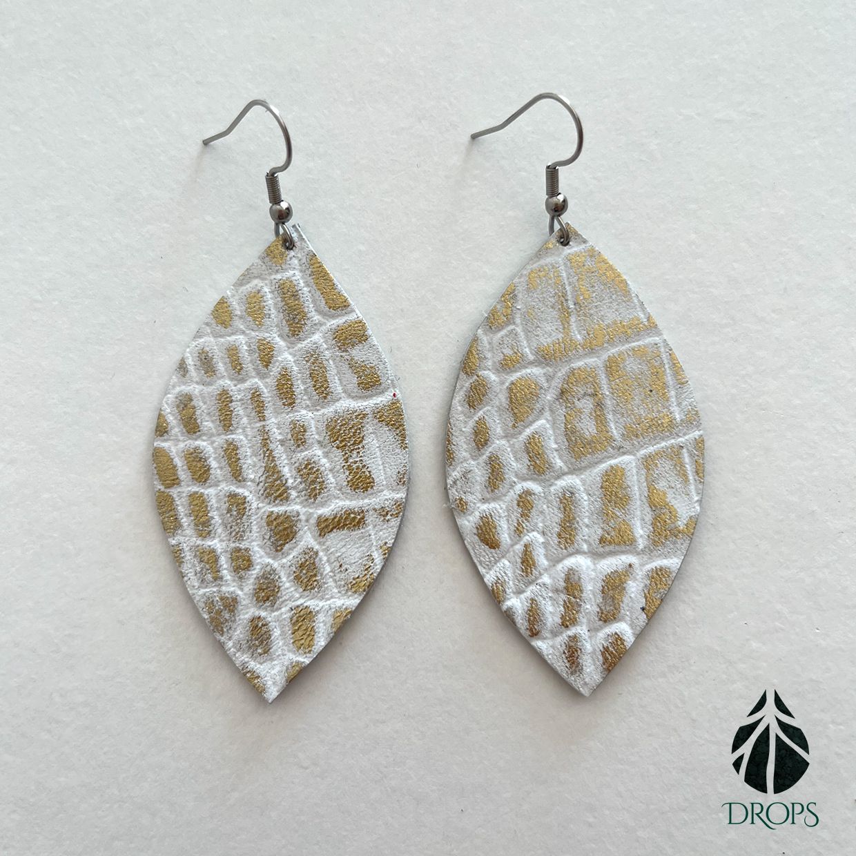 Un par de pendientes blancos y dorados hechos con gotas.