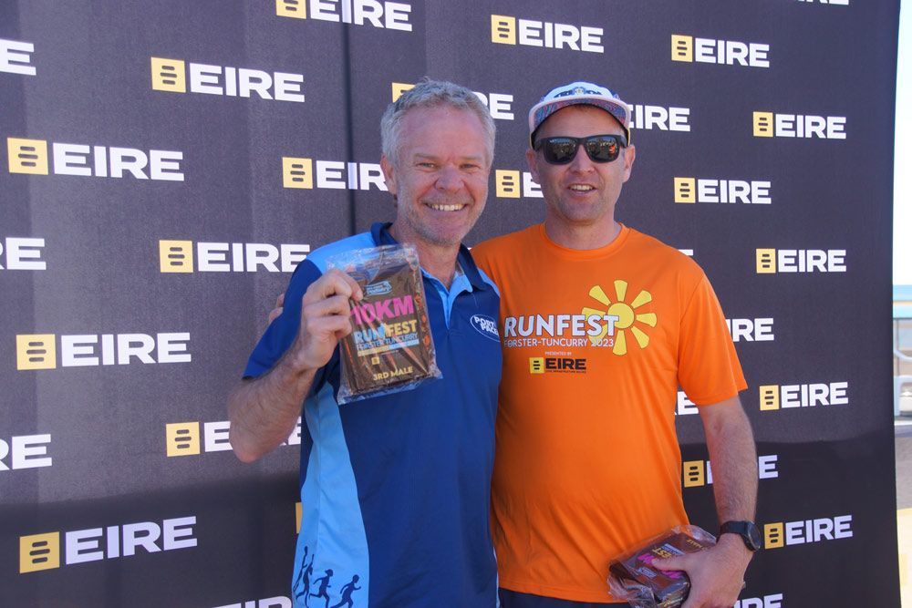 Two Men Standing In Front Of A Wall That Says Eire With 10km Trophy — Run Fest in Forster - Tuncurry, NSW