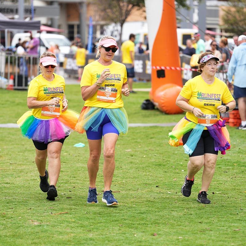 Three Women Are Running In A Park Wearing Rainbow Skirts And Yellow Shirts — Run Fest in Port Macquarie, NSW