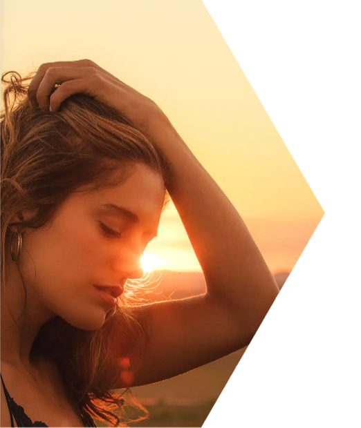 A woman is holding her hair in front of a sunset.