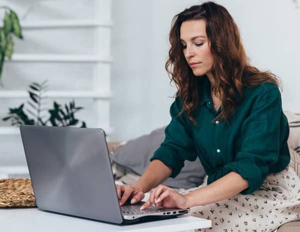 A woman is sitting on a couch using a laptop computer.