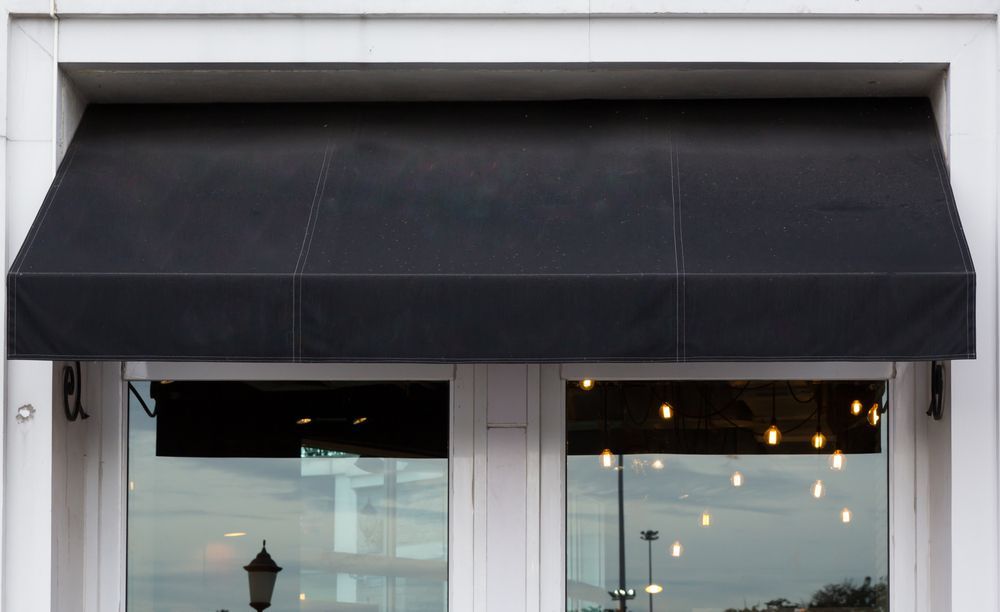 Black storefront awning above white-framed windows and glass door with warm lights inside — NT Blinds in Yarrawonga, NT
