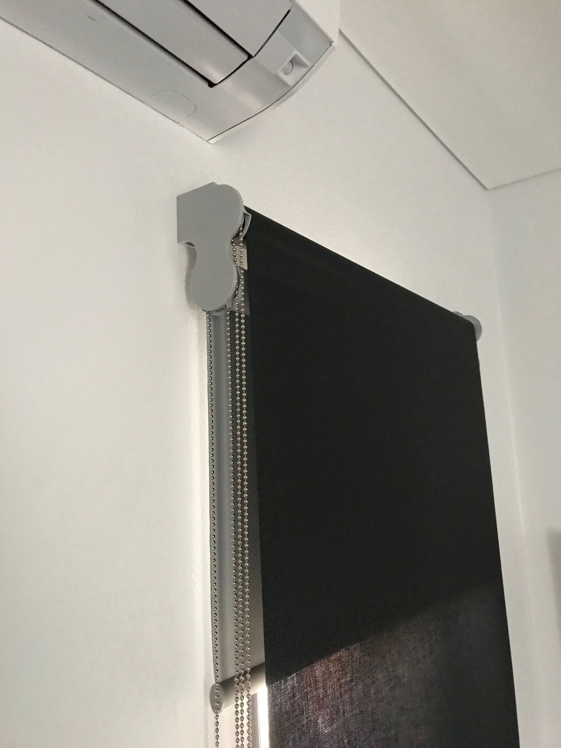 Black roller blind on a white wall with a gray air conditioner unit above — NT Blinds in Humpty Doo, NT