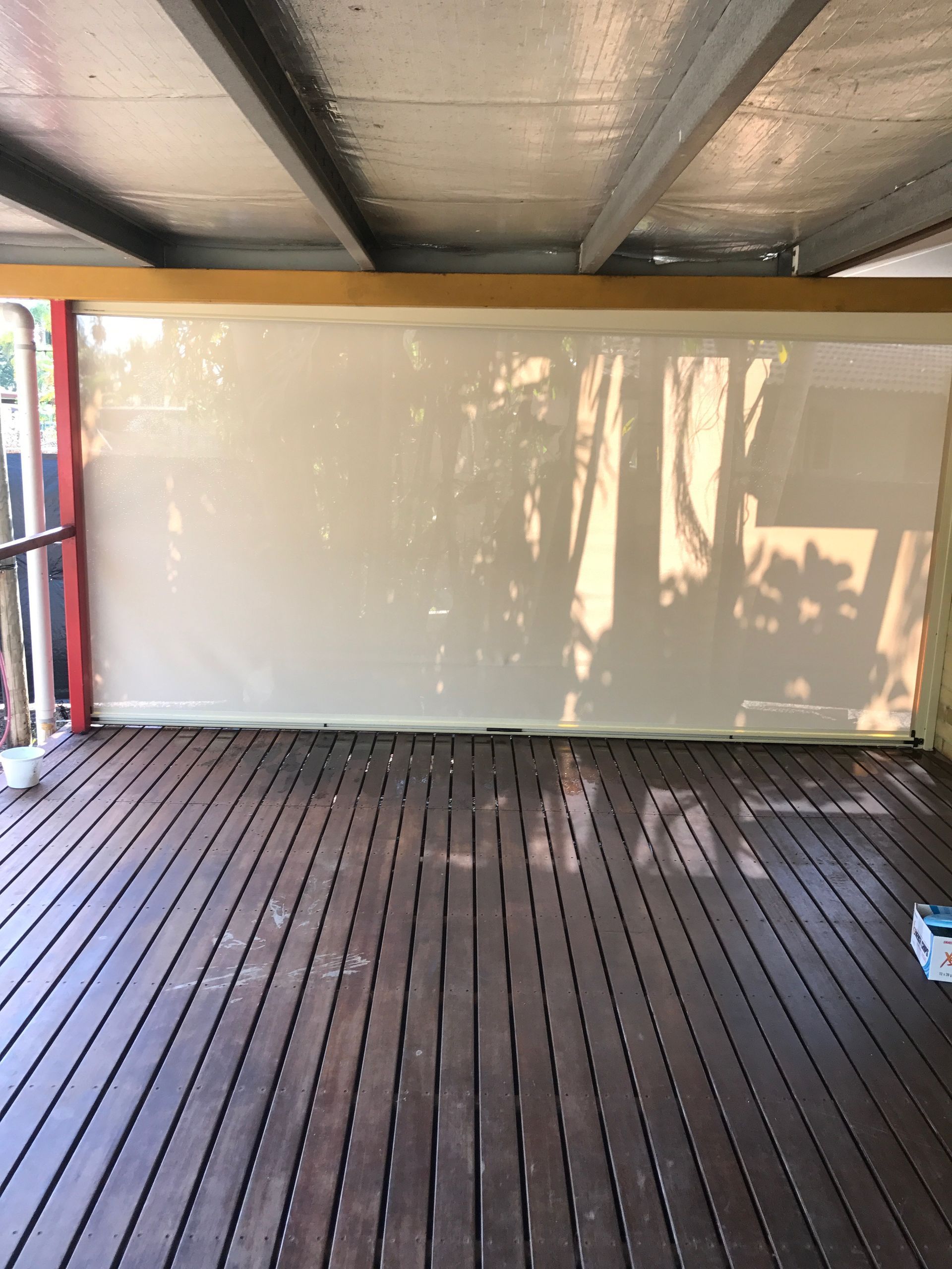 Deck with beige shade extended, shadows cast on it. Wooden deck below and a light-colored ceiling  — NT Blinds in Palmerston, NT