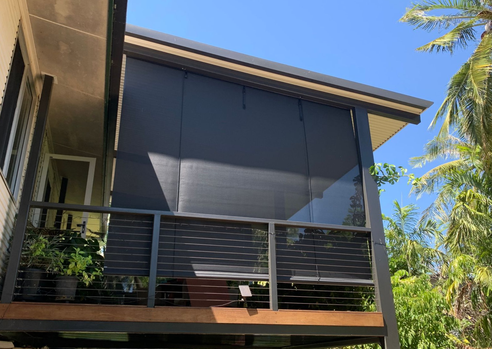 Black shade covers a deck, offering sun protection. Clear sky, wooden structure, plants visible — NT Blinds in Yarrawonga, NT