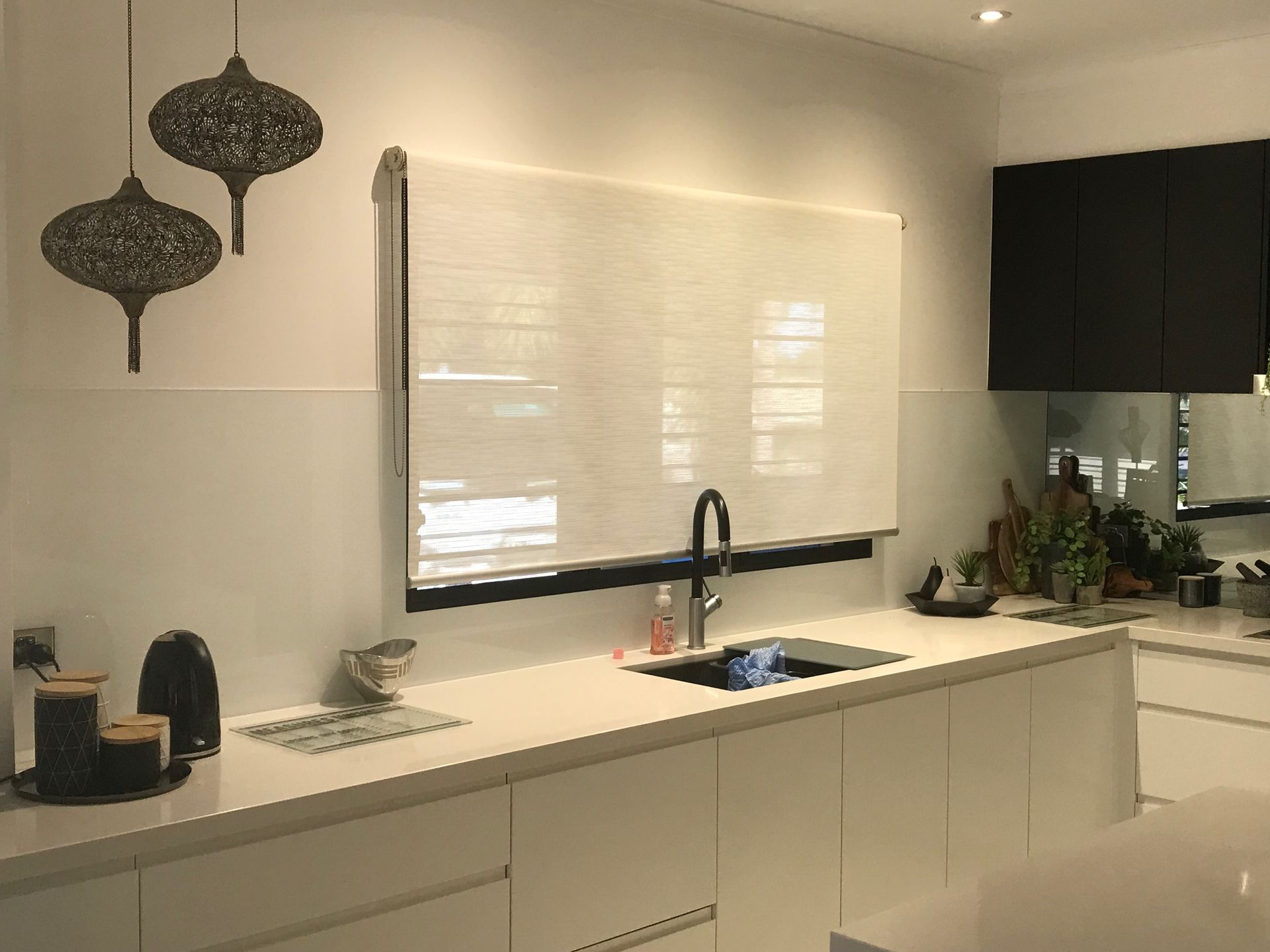 Modern kitchen with white cabinets, countertop, and a window with blinds. Two decorative lights hang above — NT Blinds in Fannie Bay, NT