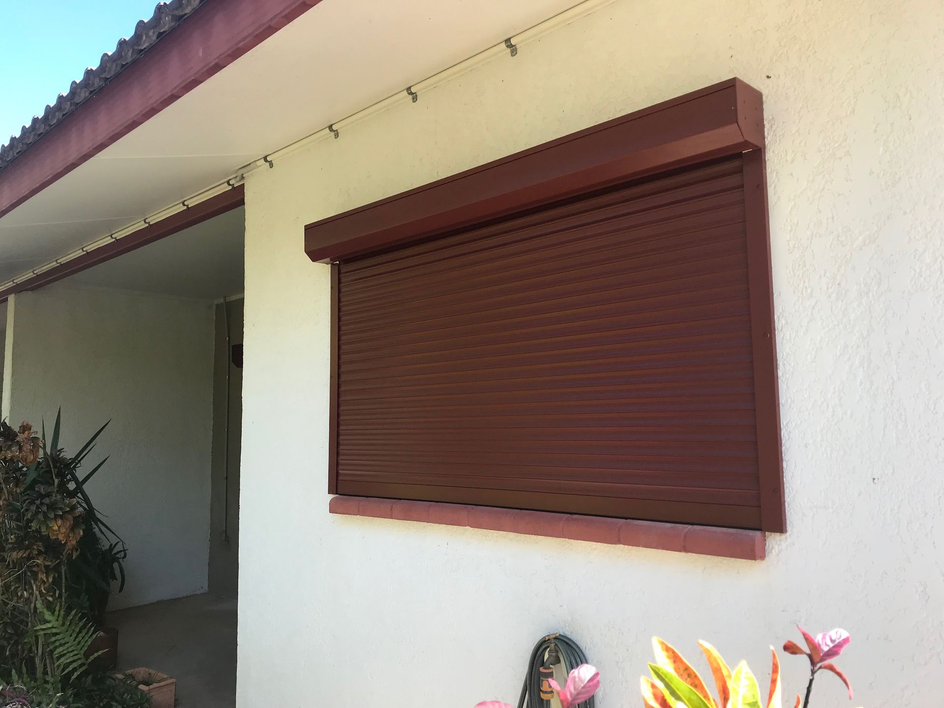 Brown closed security shutter over a window on a white building exterior  — NT Blinds in Yarrawonga, NT
