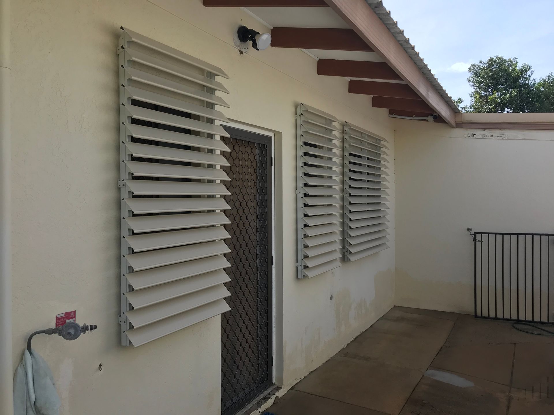 Exterior of a building with beige walls, louvered windows, and a metal security door  — NT Blinds in Yarrawonga, NT