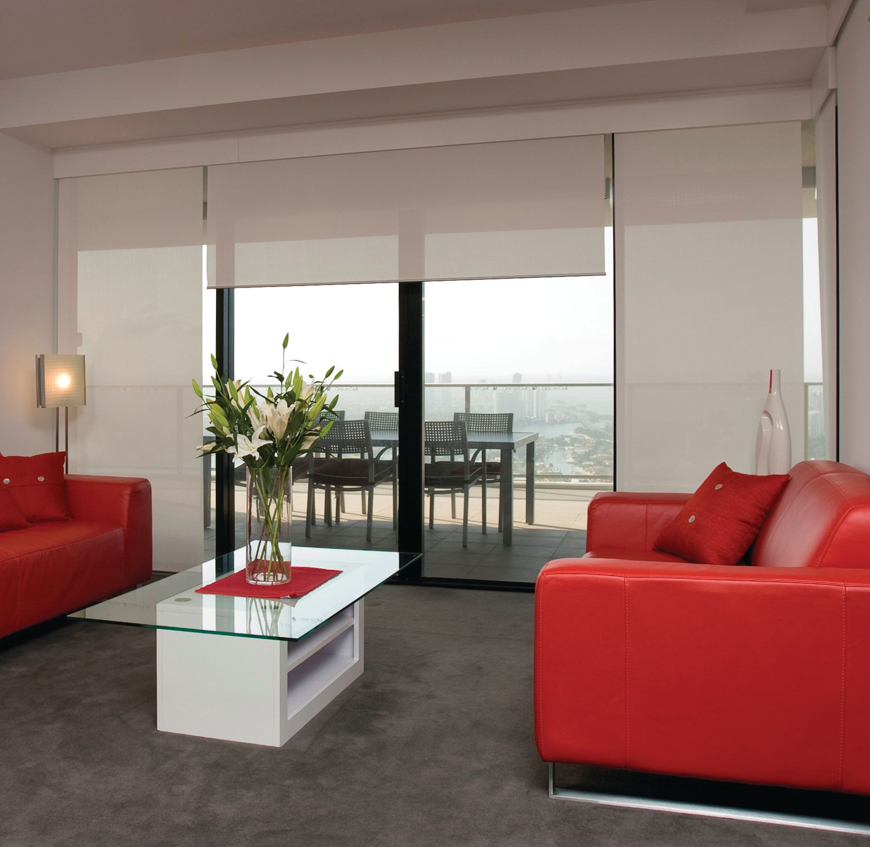 Living room with red couches, glass table, and closed white blinds overlooking outdoor dining — NT Blinds in Nightcliff, NT