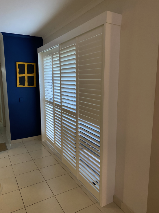White shuttered window in a room with blue and tan walls, tan tile floor, and a framed yellow and black square  — NT Blinds in Yarrawonga, NT