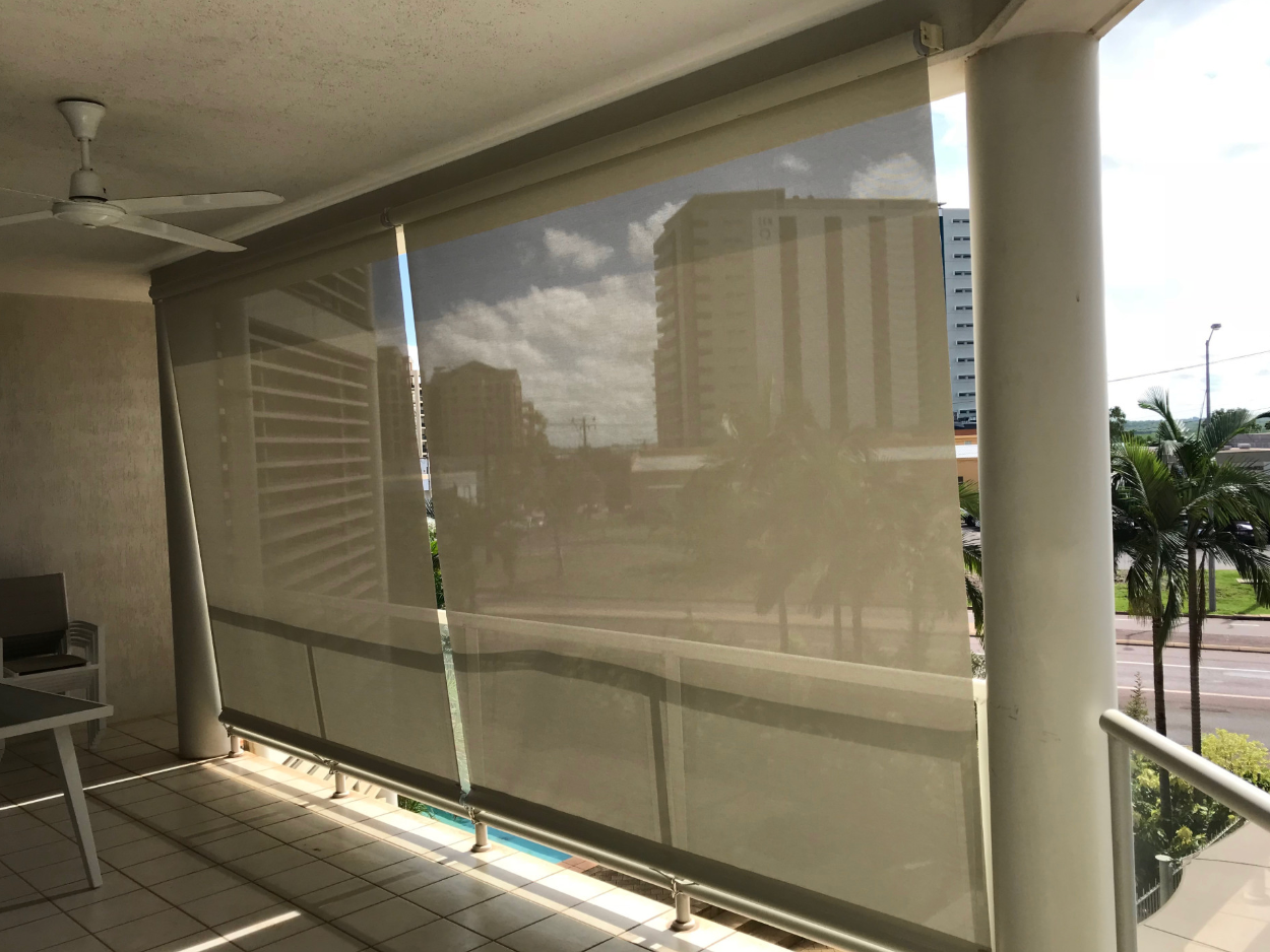 Beige sun shades on a balcony, partially obscuring the view of buildings and palm trees  — NT Blinds in Coolalinga, NT