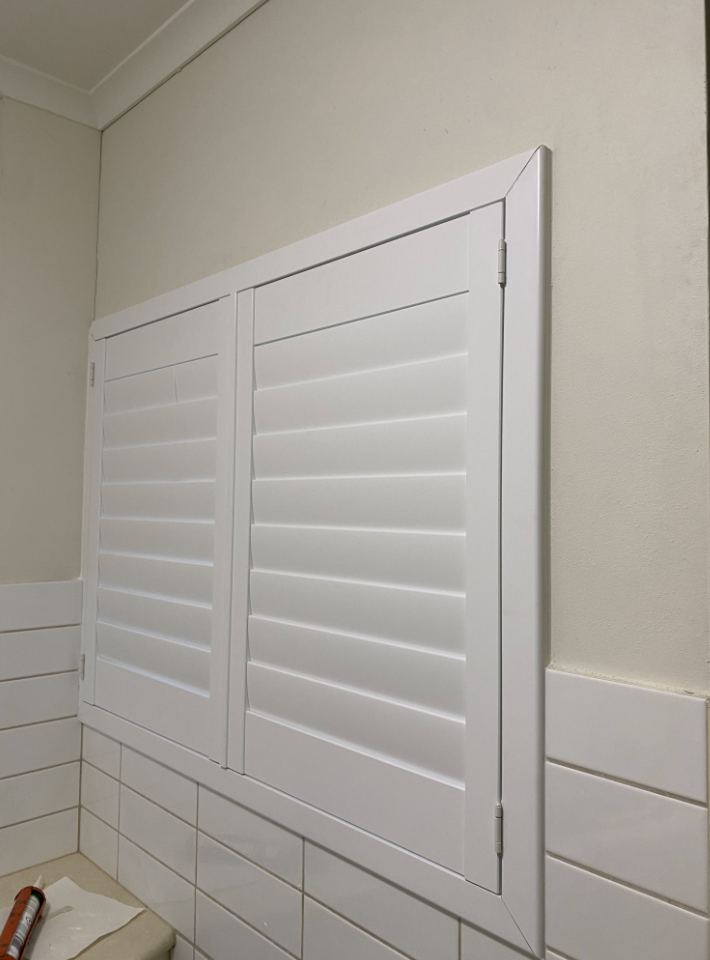 White shutters on a bathroom wall, with white tiling below  — NT Blinds in Coolalinga, NT