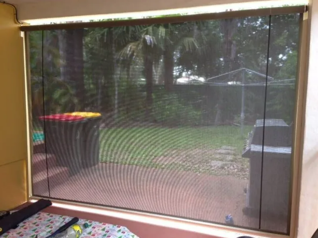 Screened Porch Window Overlooking a Backyard With Trees and a Grill — NT Blinds in Yarrawonga, NT