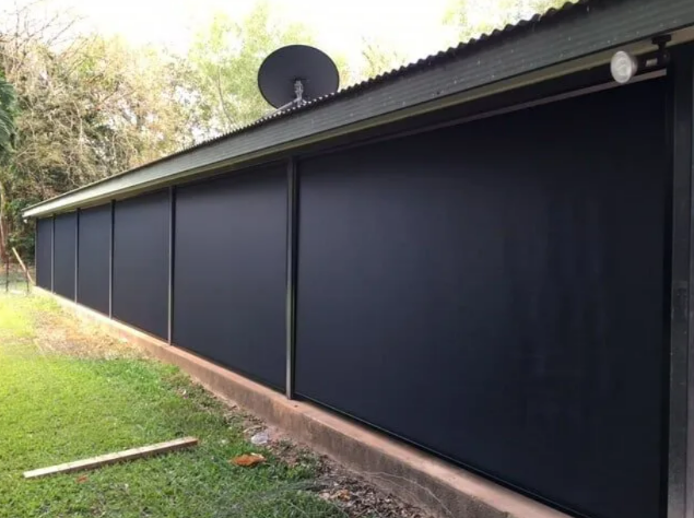 Long Black Metal Shed With Closed Roller Doors Beside a Grassy Yard — NT Blinds in Yarrawonga, NT