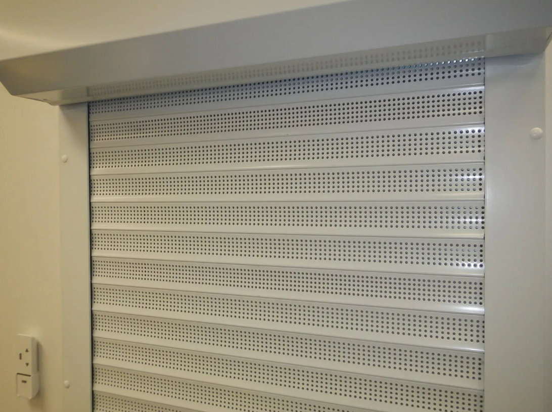 White Perforated Metal Shutter in a Beige Wall Opening — NT Blinds in Yarrawonga, NT