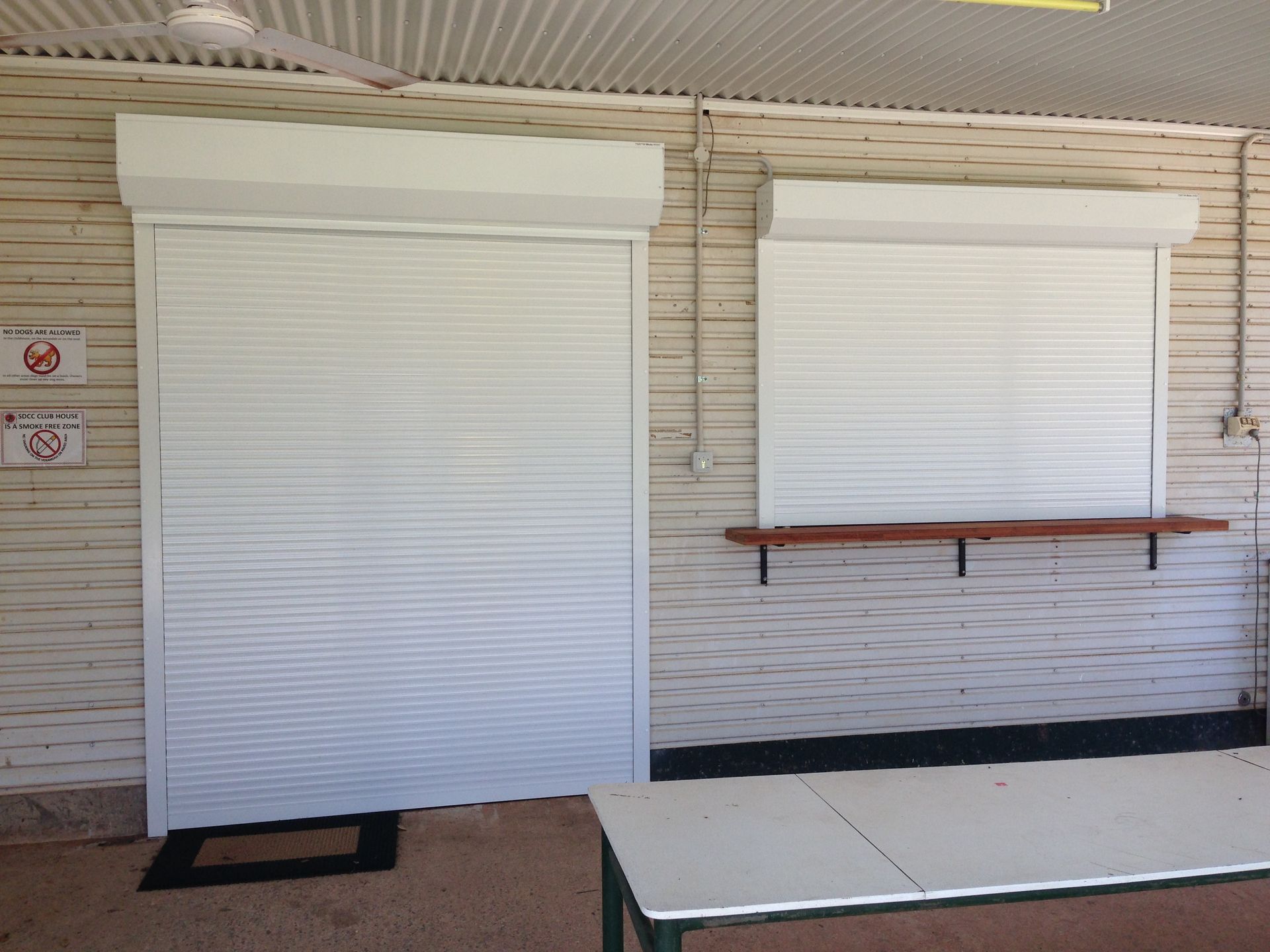 White roller shutters on a building with a table in front  — NT Blinds in Yarrawonga, NT