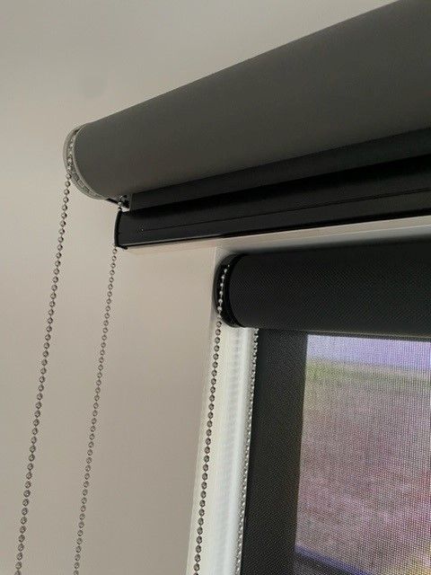 Two roller blinds: gray top, black bottom, with silver beaded pull cords, mounted on a white wall  — NT Blinds in Yarrawonga, NT
