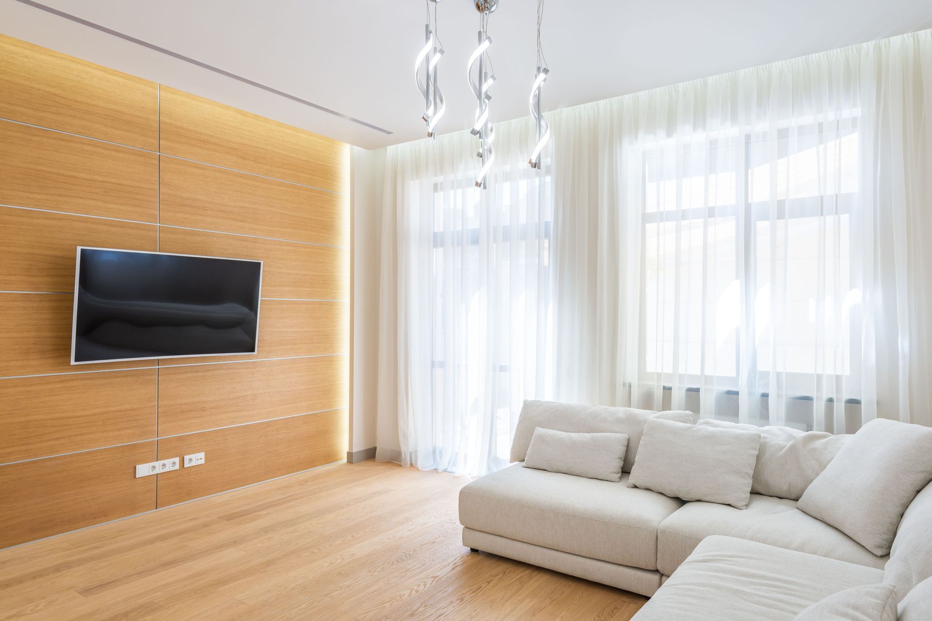 Modern living room with a wall-mounted TV, white sectional sofa, and large sheer curtains — NT Blinds in Yarrawonga, NT