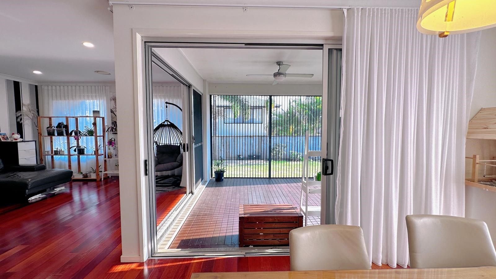 Covered outdoor patio with wooden floor, overlooking a backyard with green grass, fences, and trees  — NT Blinds in Yarrawonga, NT