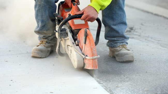 Worker using a concrete saw to cut pavement along a fresh white curb line