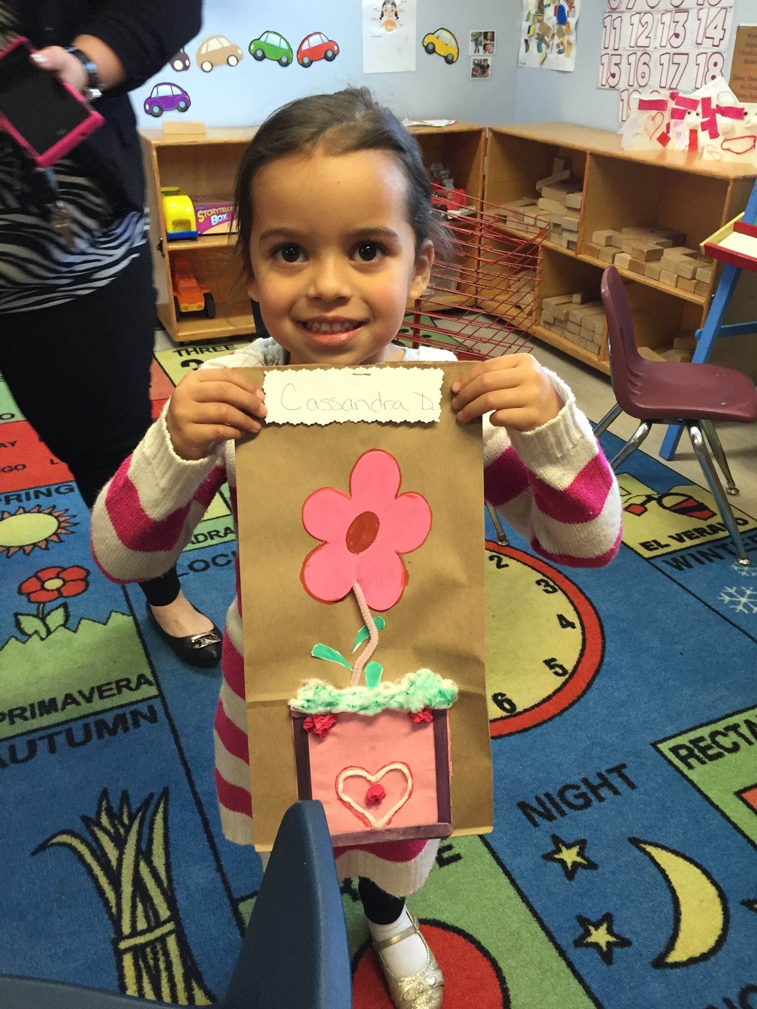 A little girl is holding a paper bag with a flower in it.