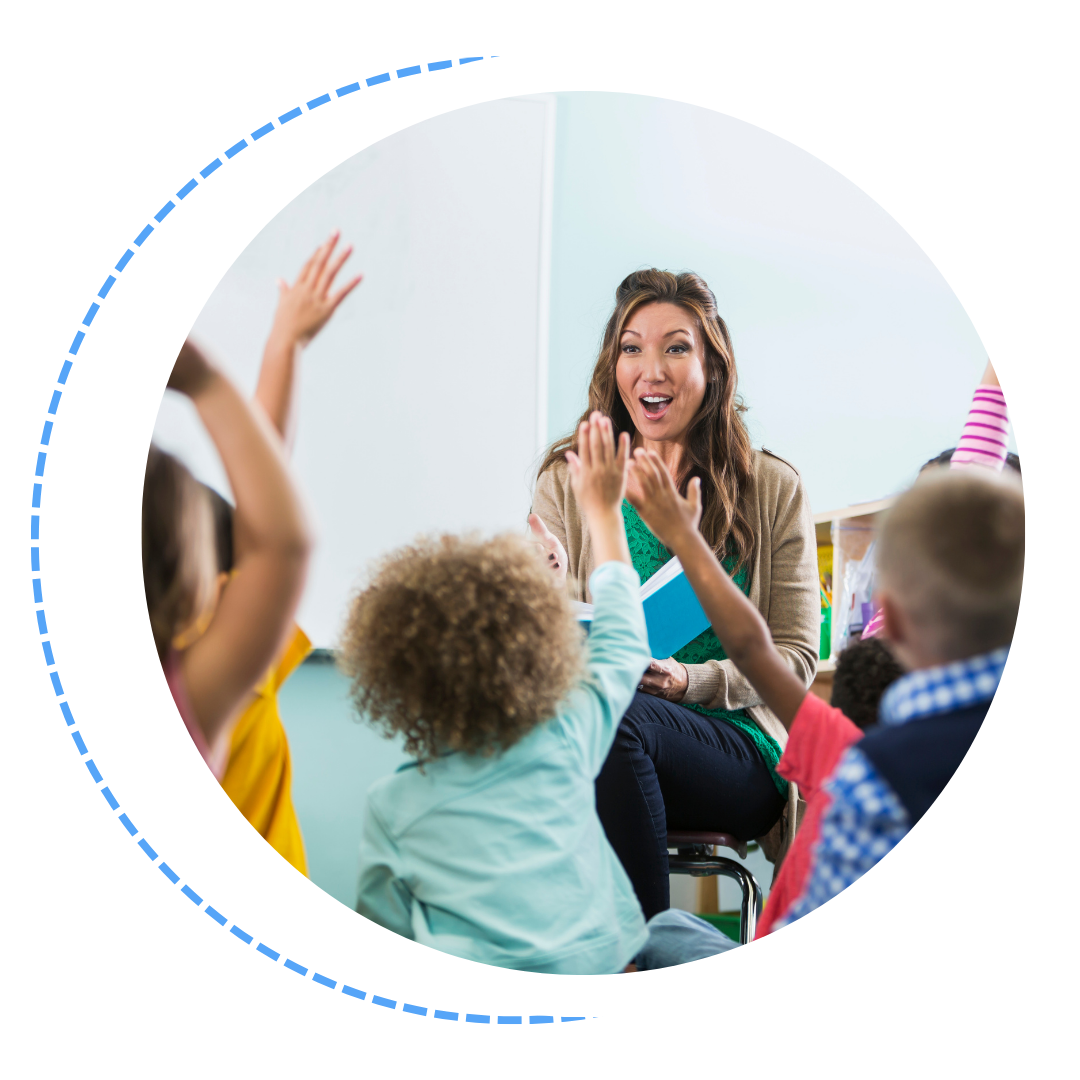 A teacher is sitting in front of a group of children raising their hands.