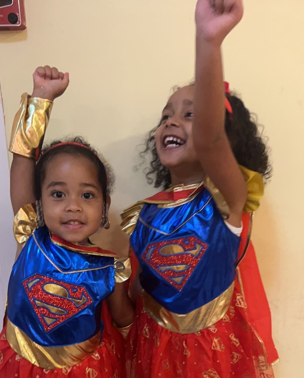 Two little girls dressed in superman costumes with their arms in the air