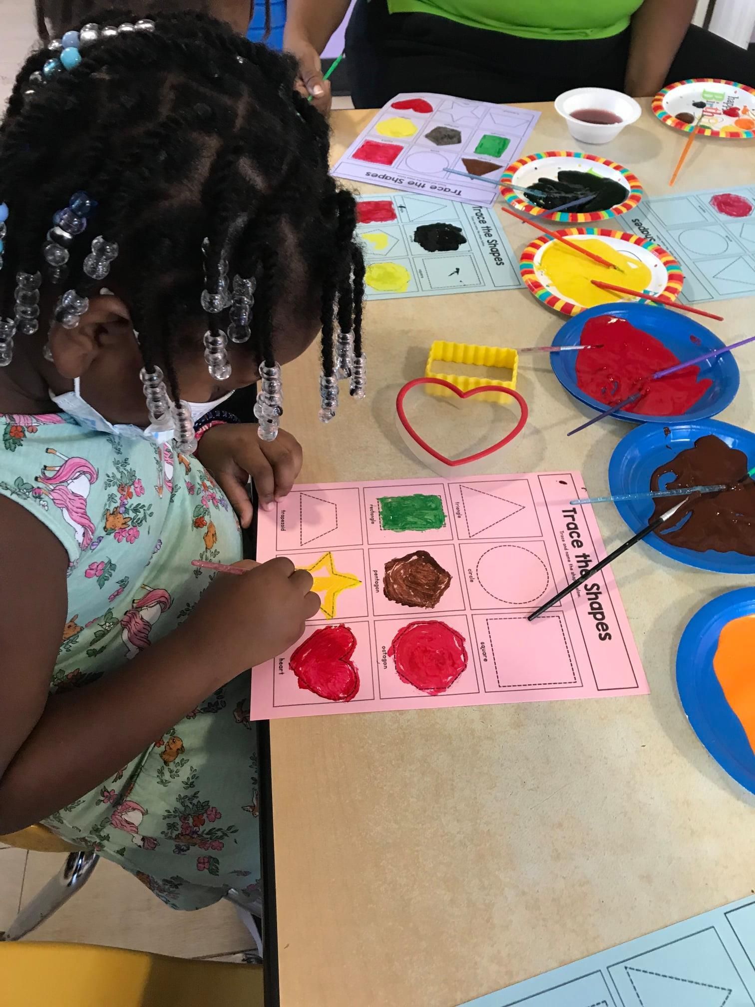 A little girl is sitting at a table painting on a piece of paper