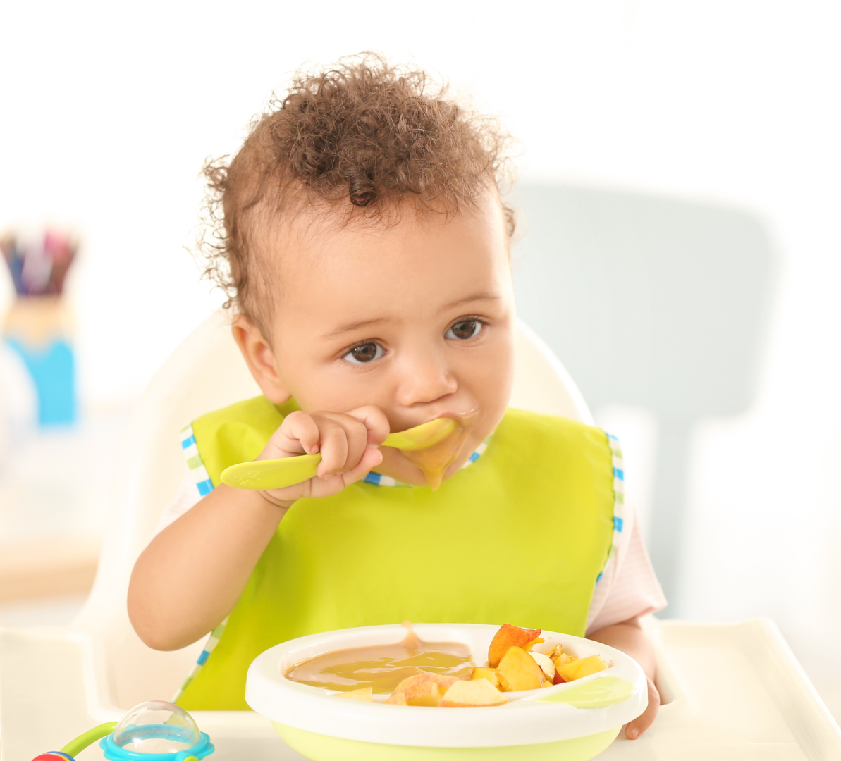 A baby is eating food from a bowl with a spoon.