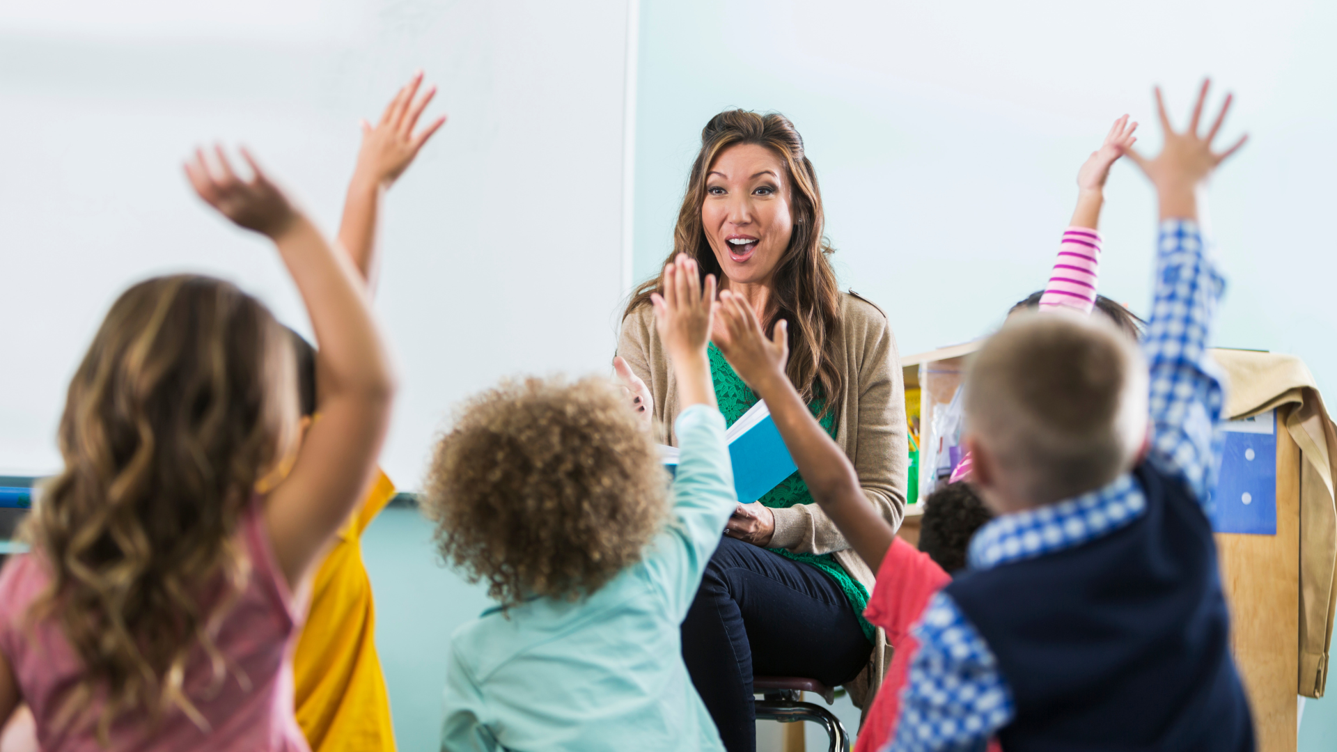 A group of children are raising their hands to answer a question in a classroom.