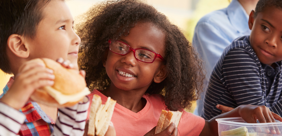 A group of children are sitting at a table eating food.