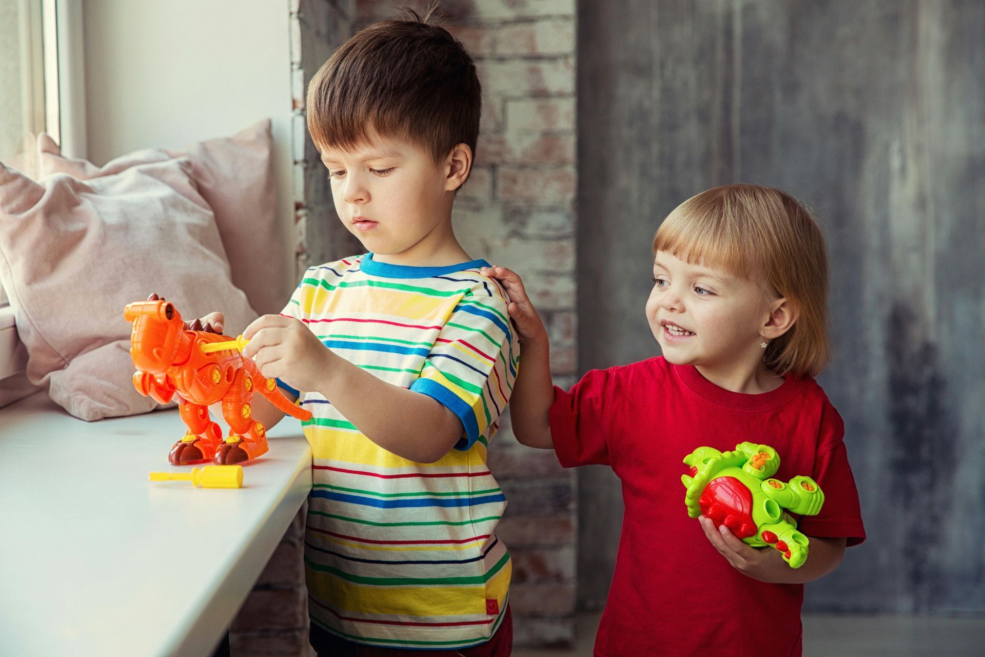 A boy and a girl are playing with toys on a window sill.