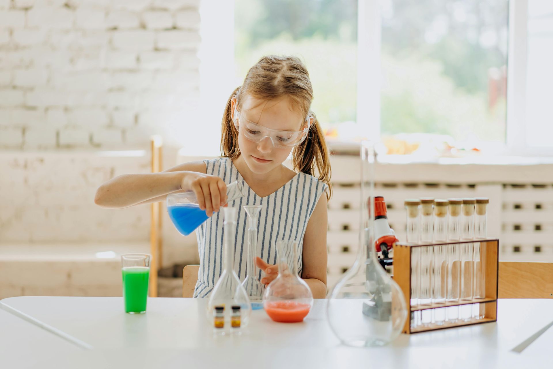 A young girl is sitting at a table pouring liquid into a beaker.