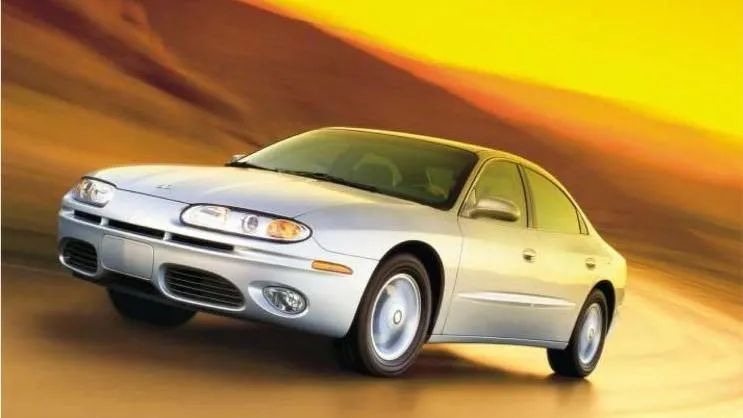 Silver Oldsmobile Alero sedan driving on a blurred, yellow background.