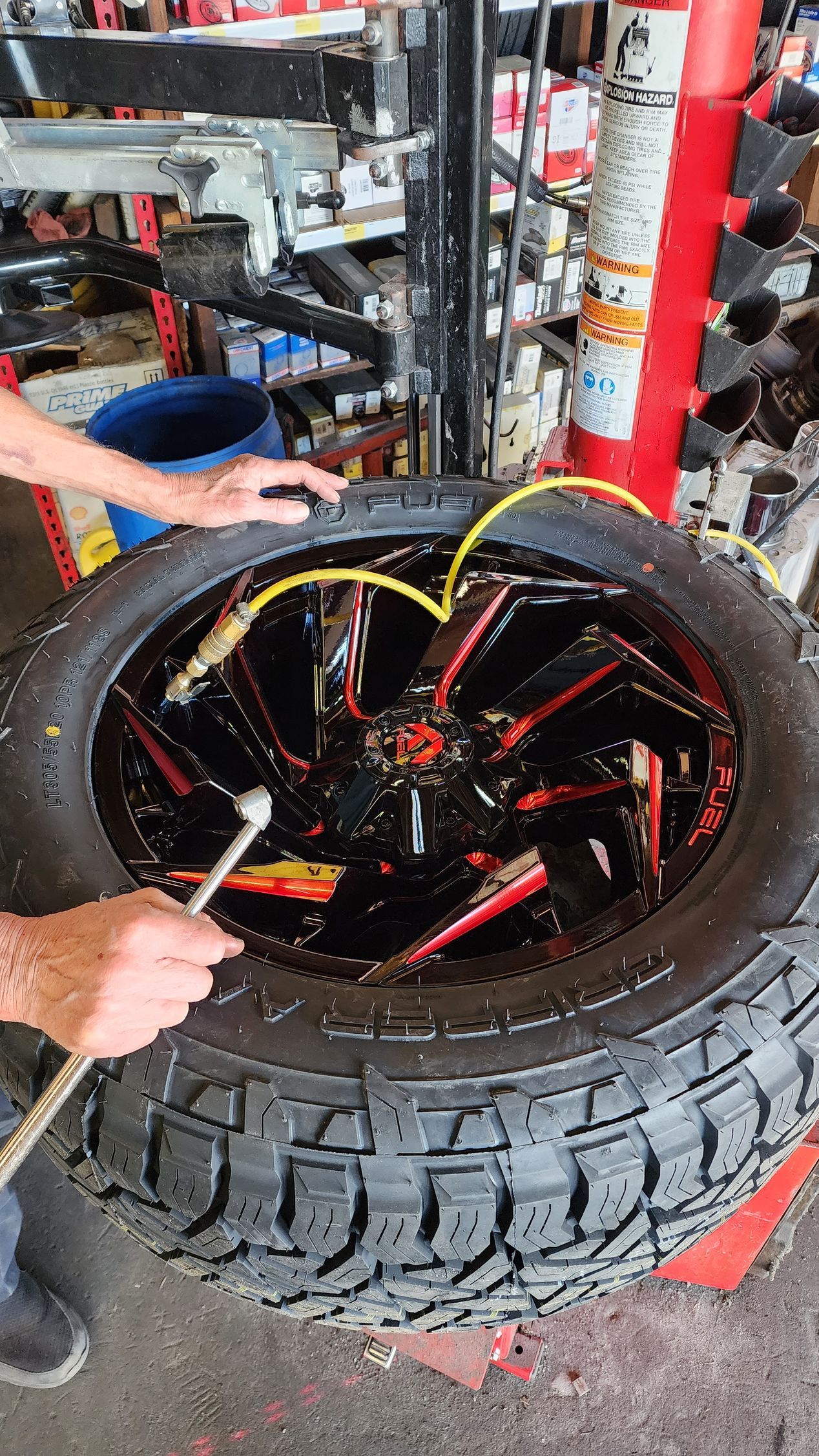 Man working on a tire with red and black rim, yellow tubes, and tools in a shop.