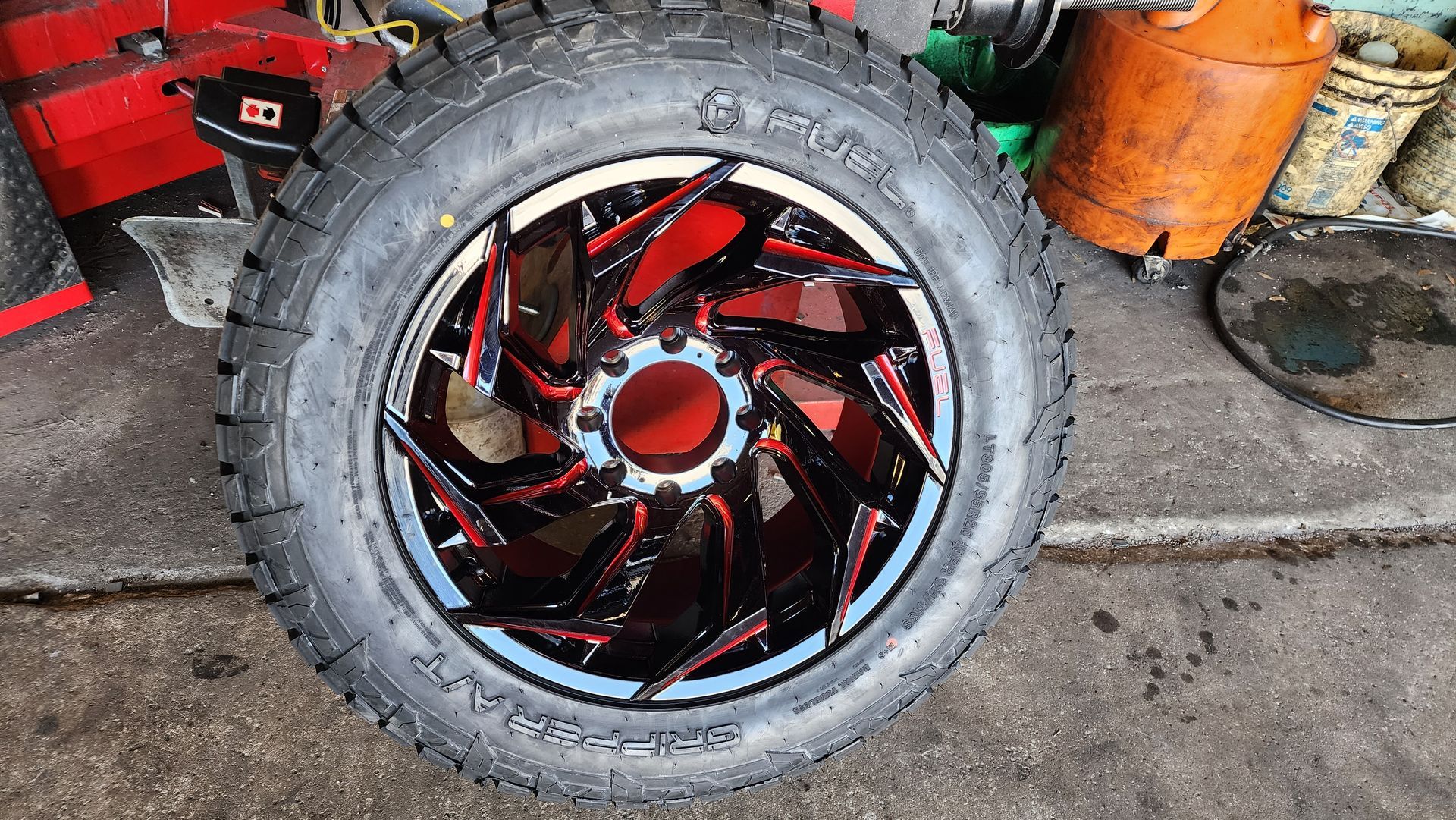 Black and red custom truck wheel with a thick tire, in a mechanic's shop.