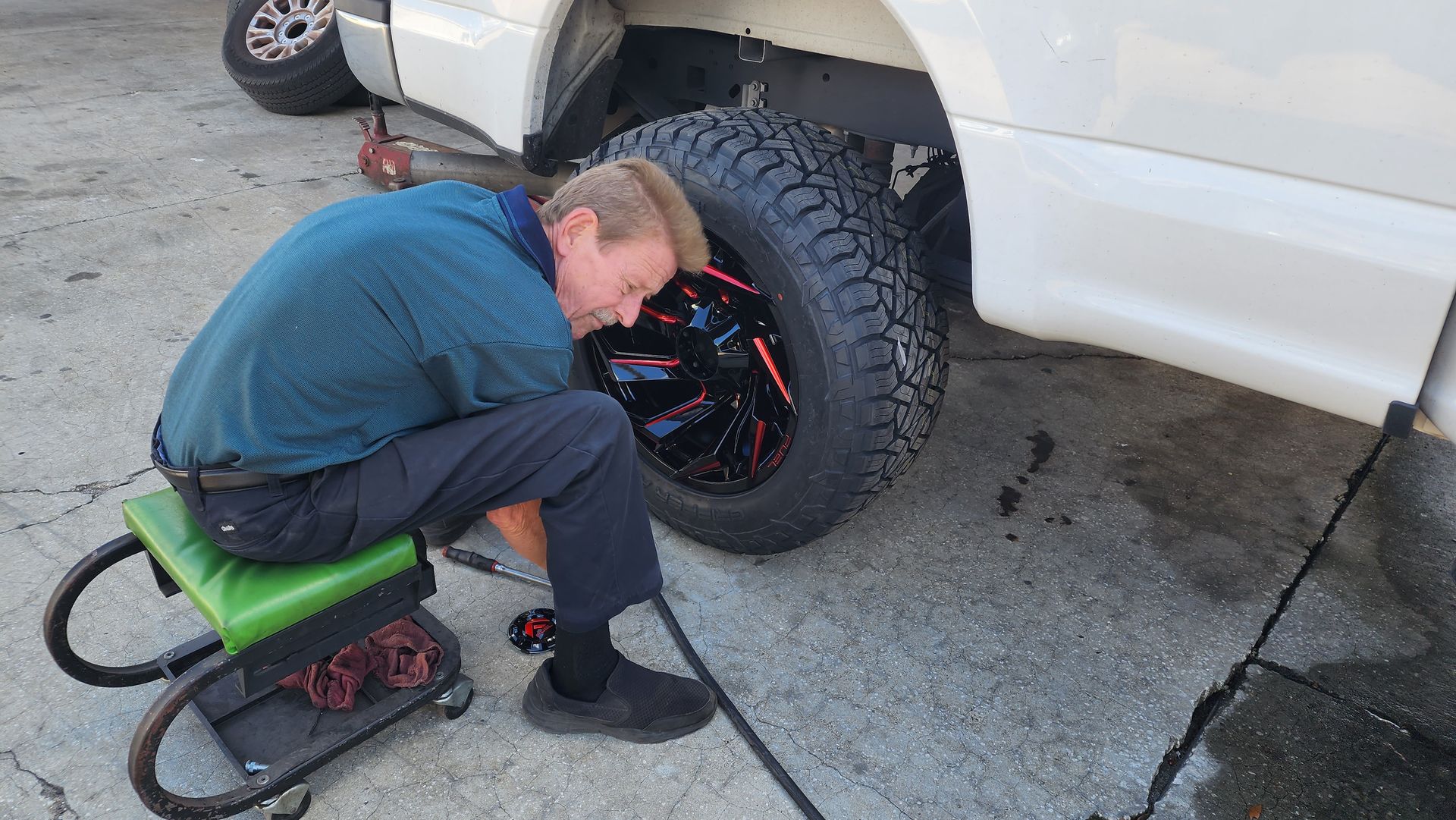 Man on rolling stool changing a tire on a white truck.