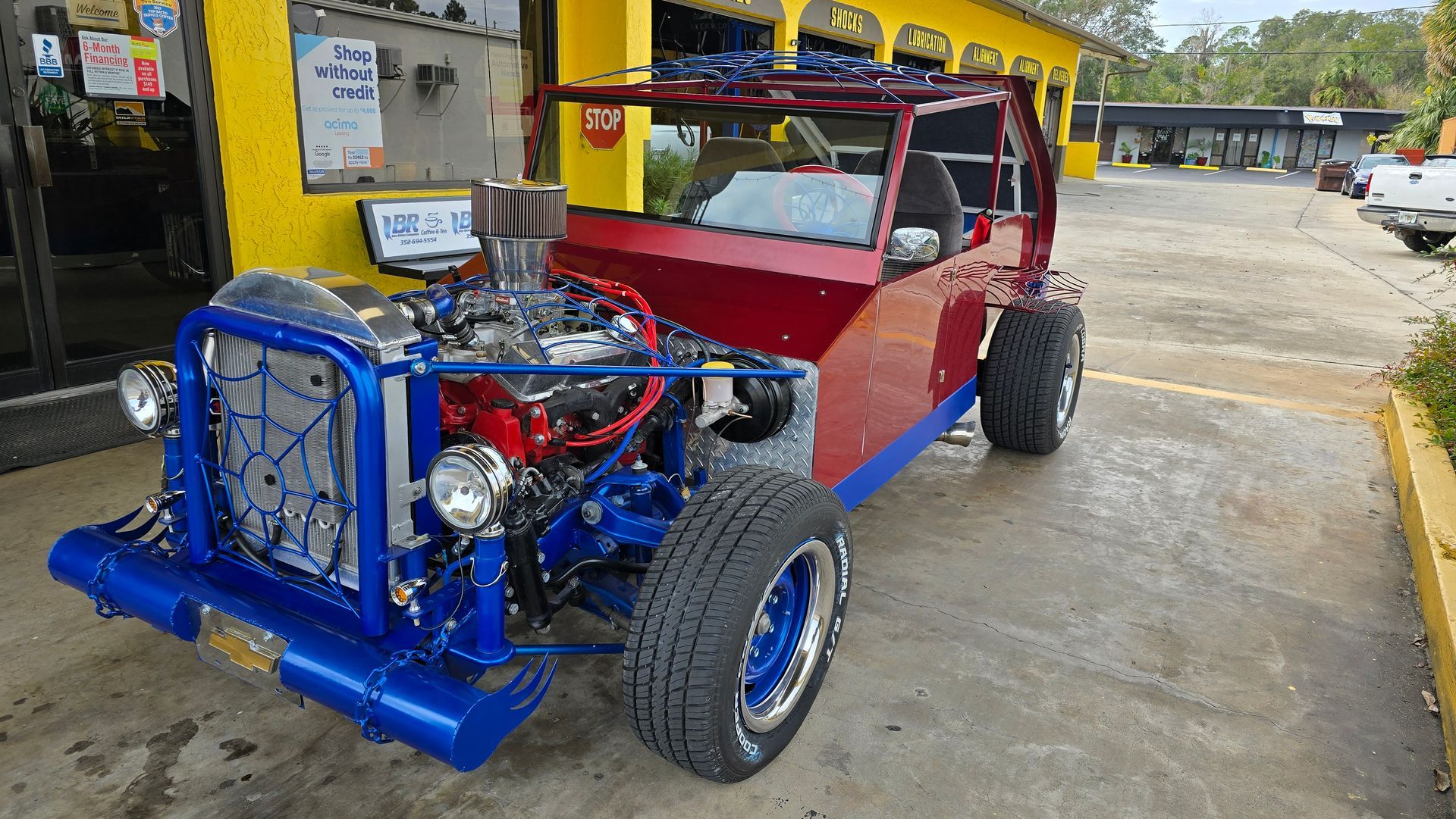 Custom red and blue car with large engine in a gas station.