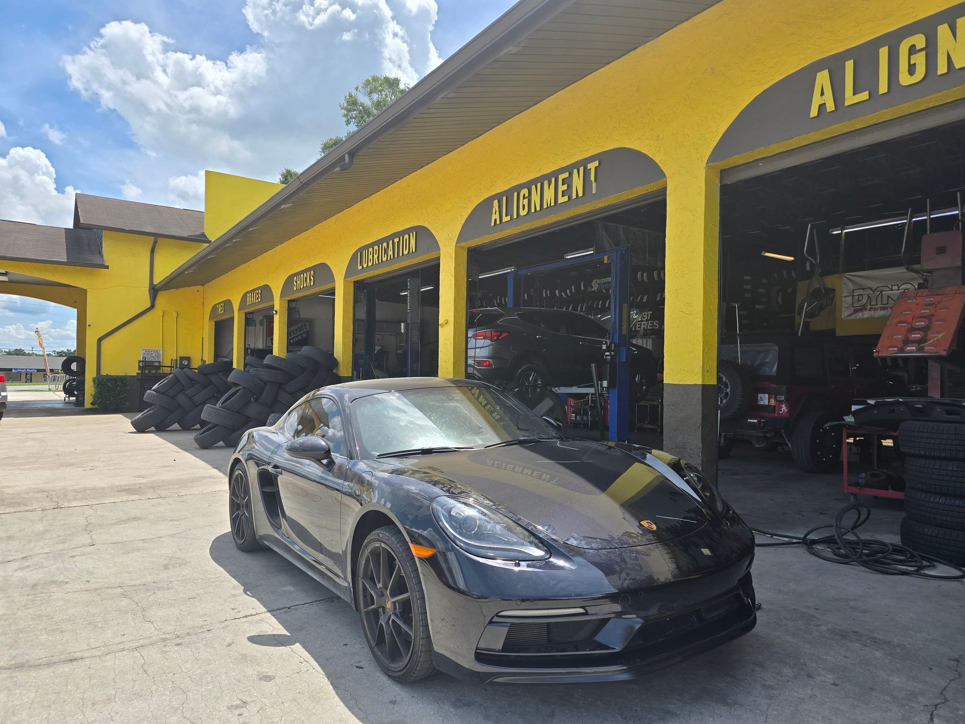 Black Porsche in front of a yellow auto shop with the word