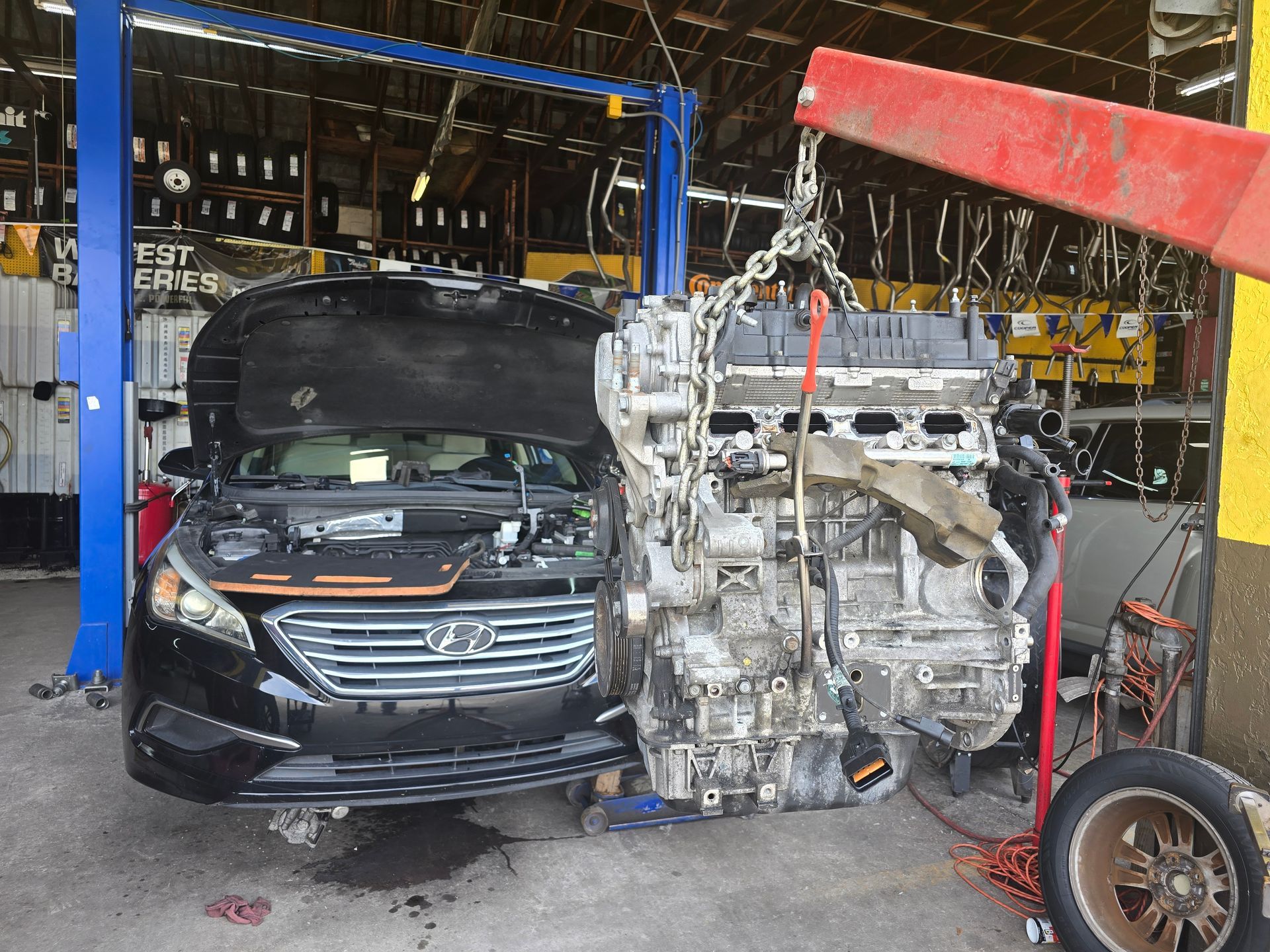 Car engine being lifted out of a black car at an auto repair shop.