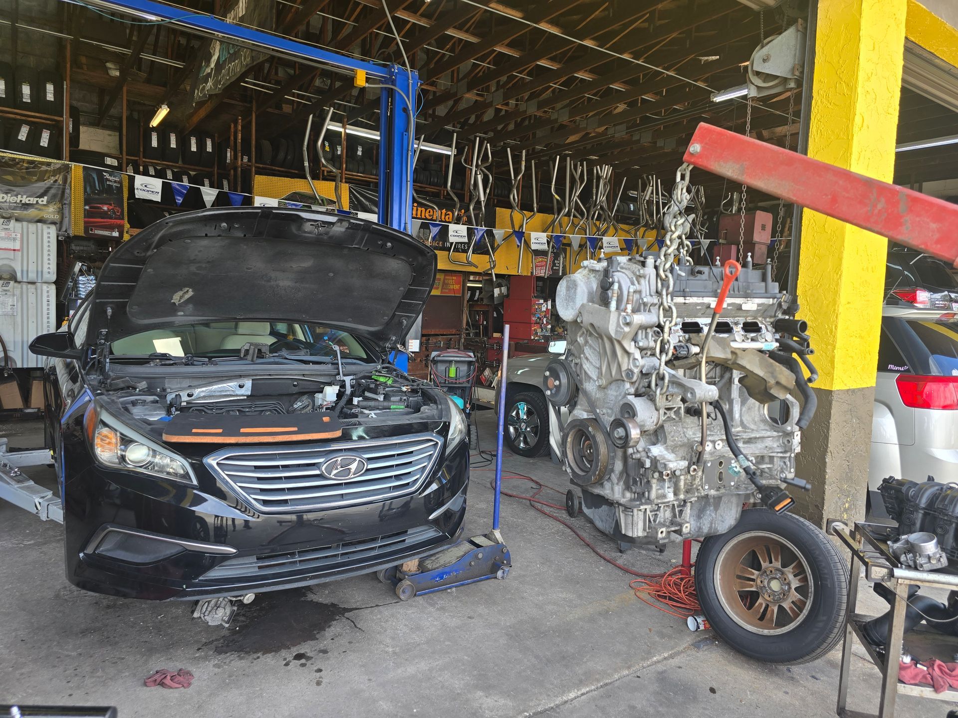 Car in auto repair shop, engine being removed, tools and parts visible.