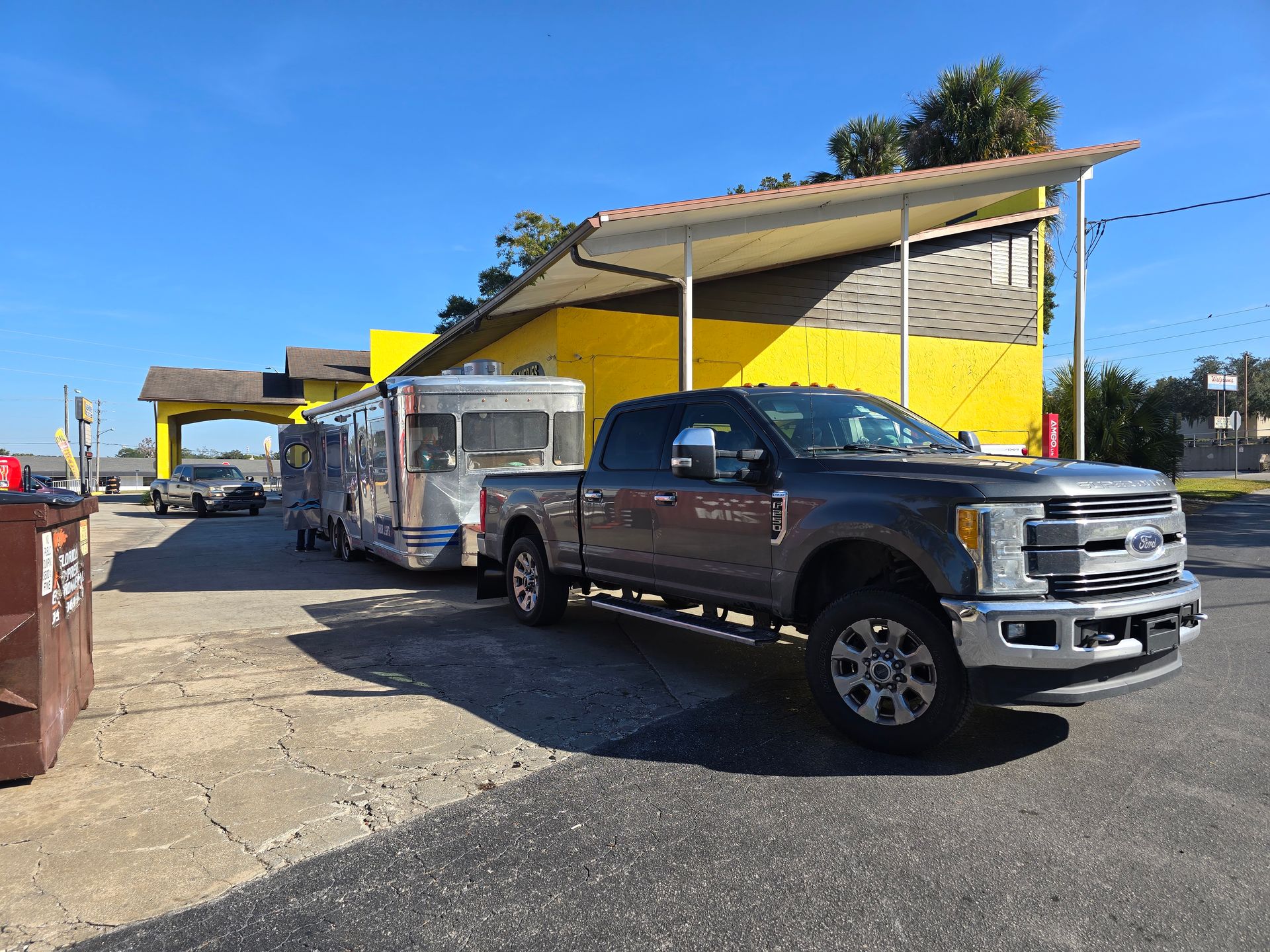 Gray truck towing a silver trailer parked under a yellow canopy; sunny day.