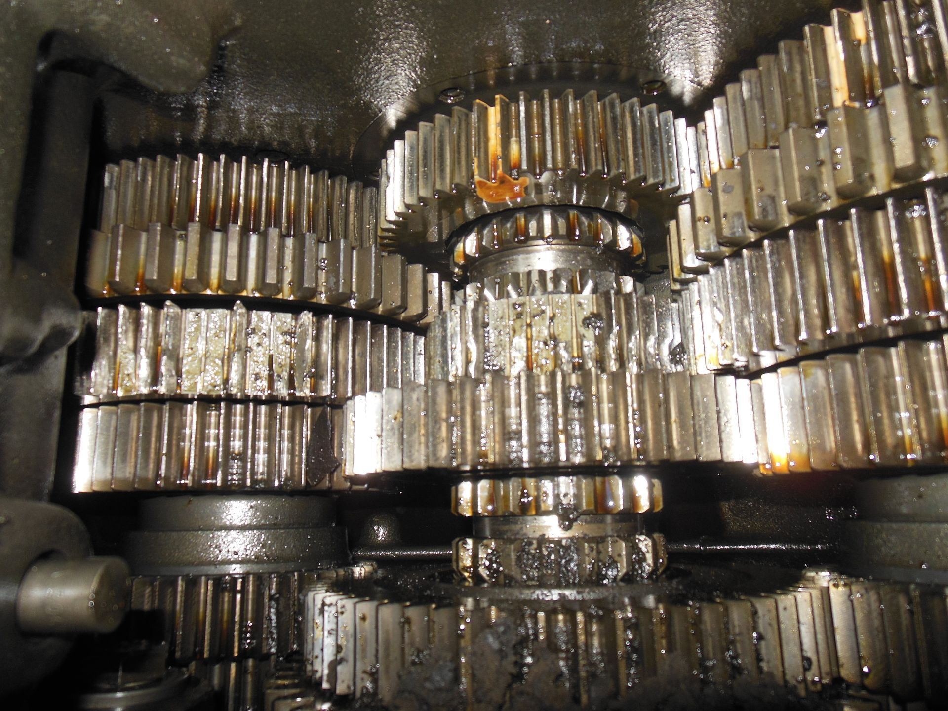Gears meshing together inside a machine, covered in oil, in a dark setting.