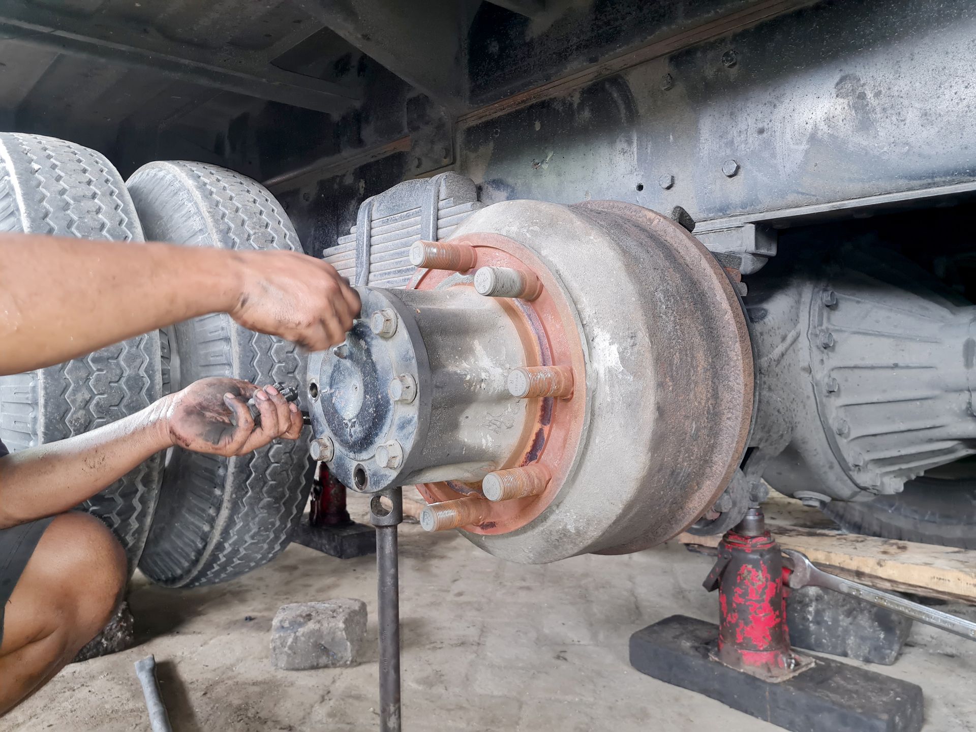 Mechanic working on a truck's wheel and brake assembly.  Gray, black, and red components.  Hands are visible.