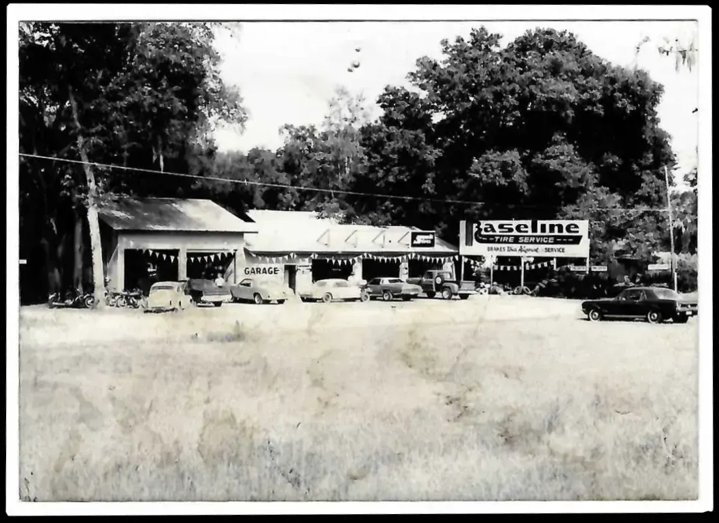 Vintage black and white photo of a gas station and cars lined up, with a 
